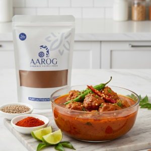 Aarog Zesty Authentic Achar Gosht Masala recipe mix pouch next to a bowl of finished Achar Gosht curry.